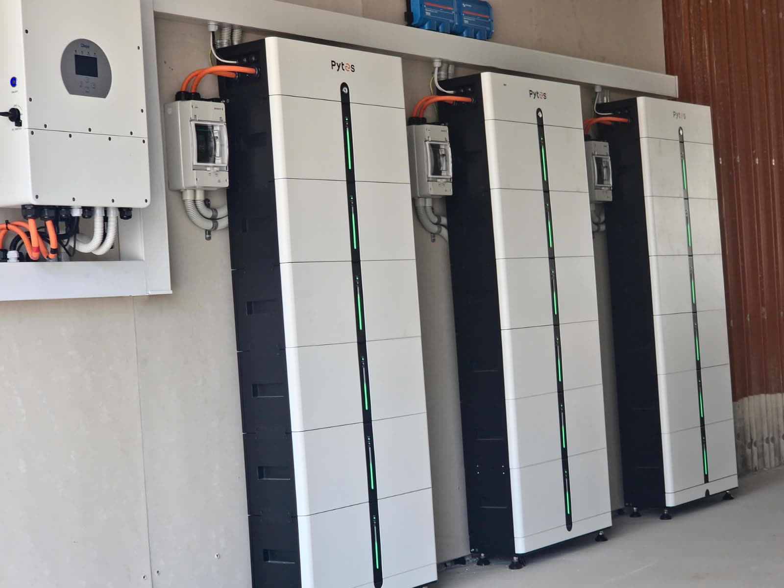 Outdoor wall-mounted Deye inverter with a Pytes Pi LV1 battery stack on a rendered wall